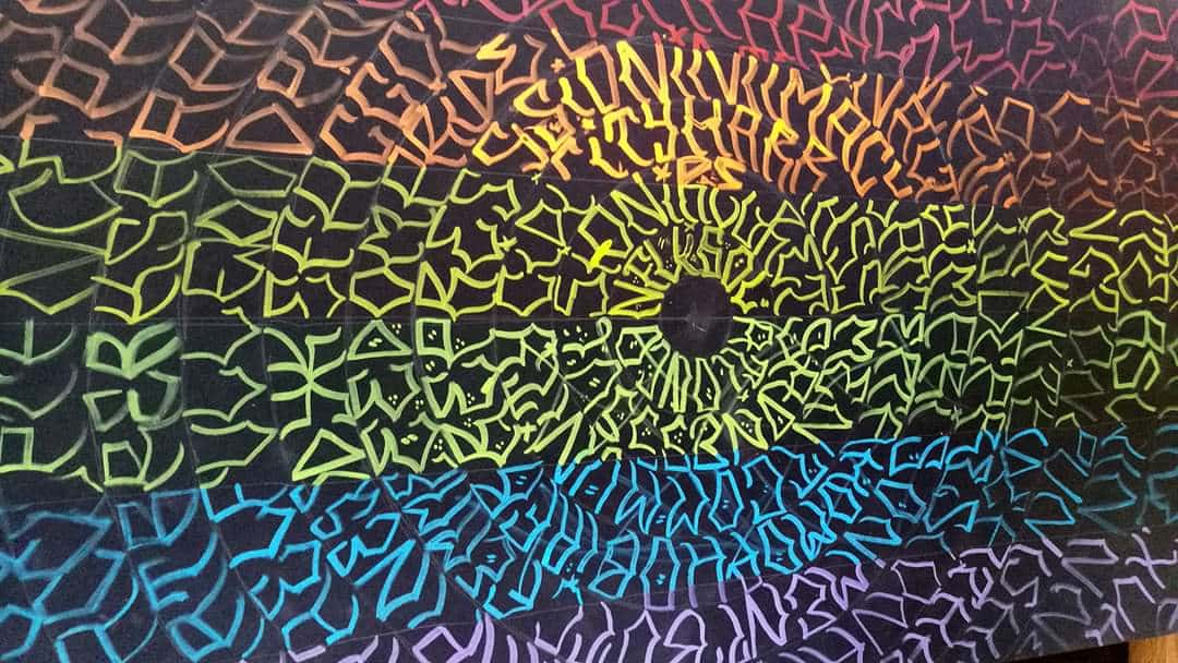 A long rectangular painting made from script writing in a circular design drawn in the colours of the rainbow to imitate the flag associated with LGBT pride 