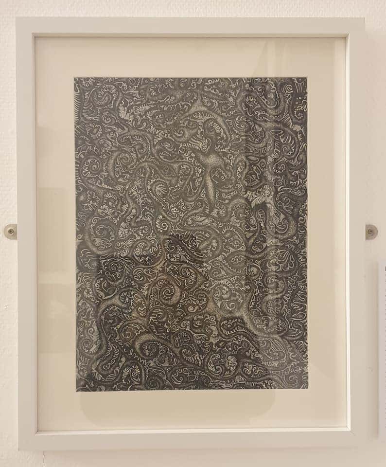 A drawing in black ink made from tiny highly detailed swirls and patterns, covering a large sheet of paper and framed in a white box frame